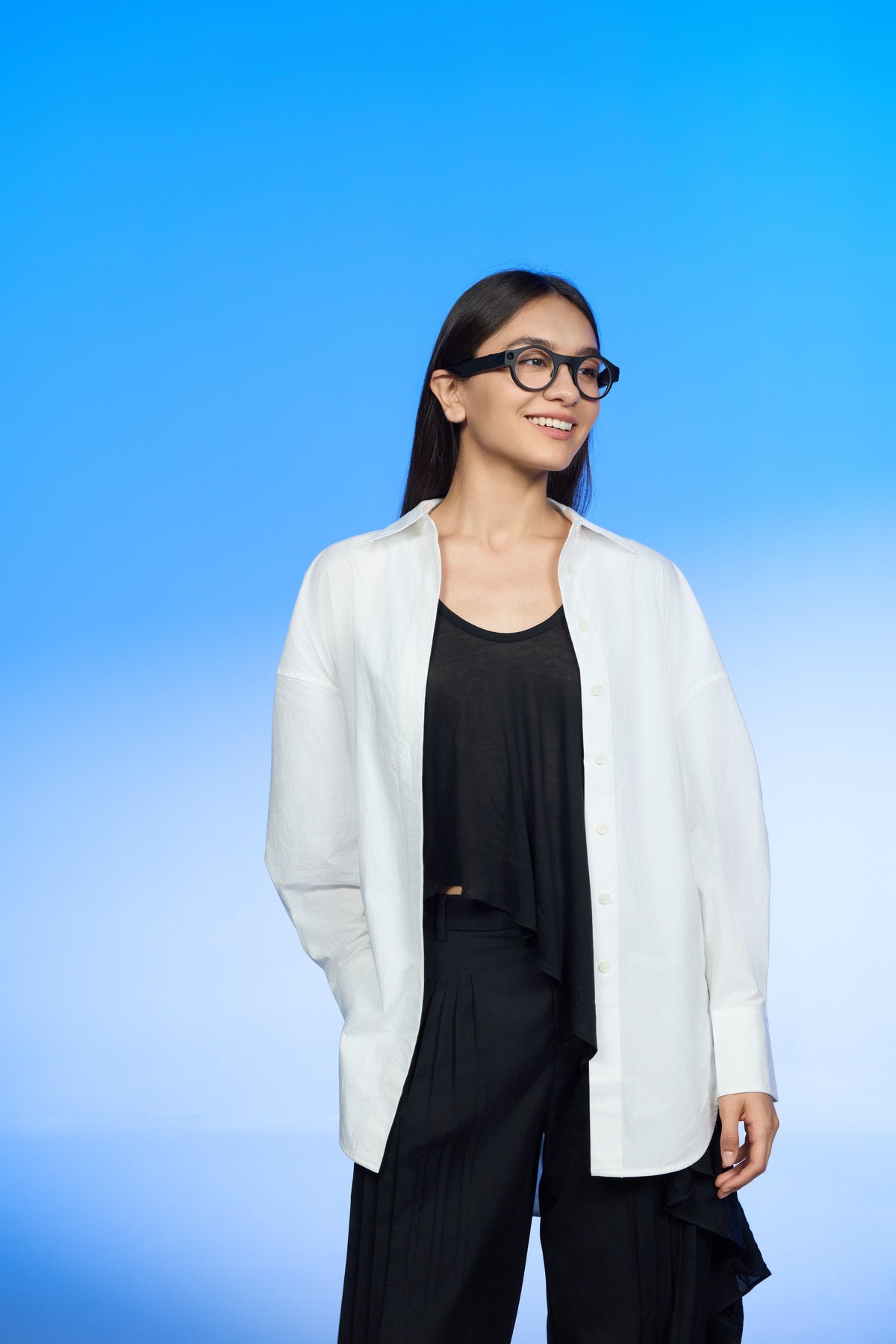 Female model wearing 8ight camera glasses with a clear-lens look on a blue studio gradient, full-body walking portrait.