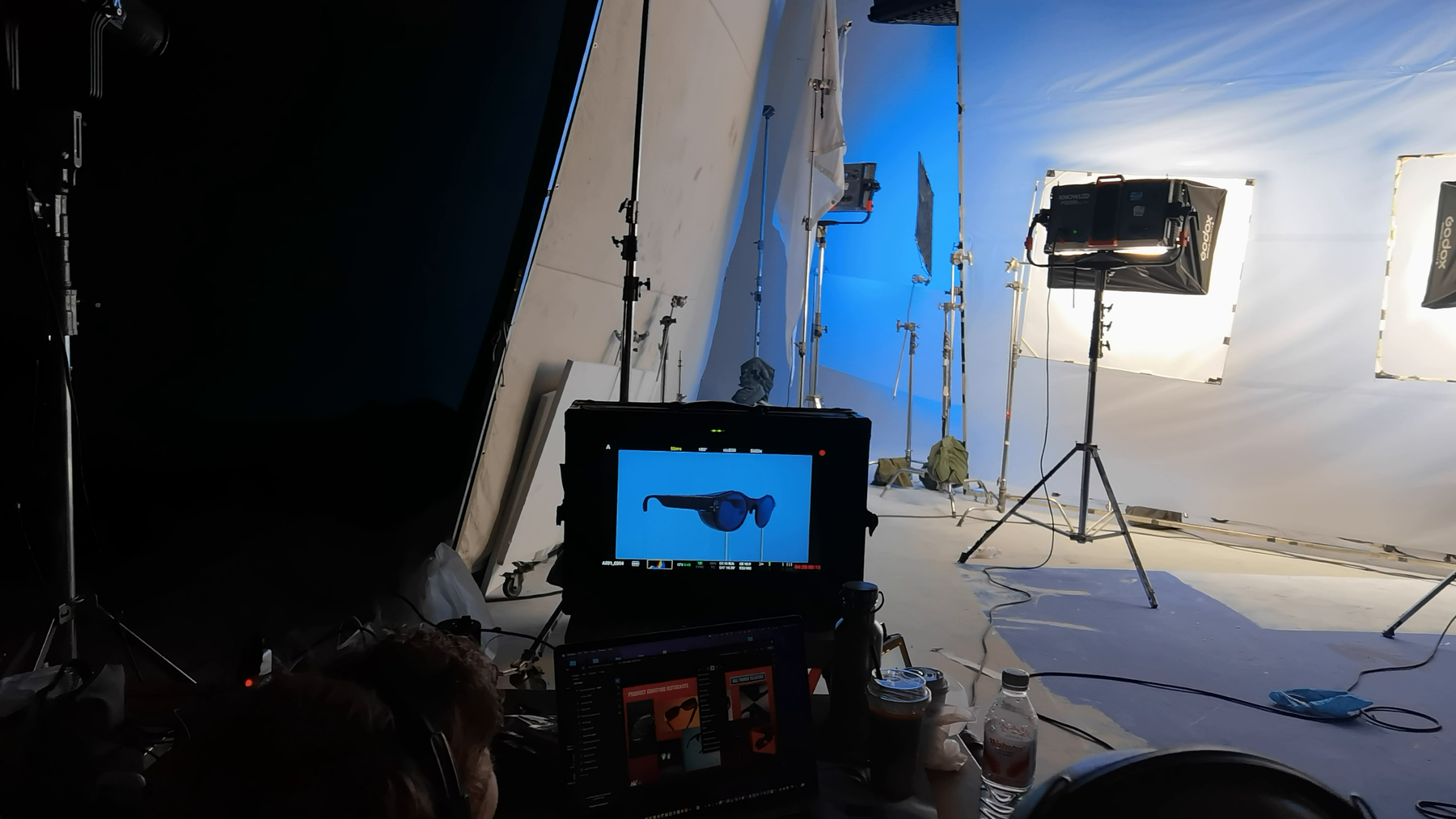 Production monitor displaying dark 8ight camera glasses in front of a brightly lit white-and-blue studio set.