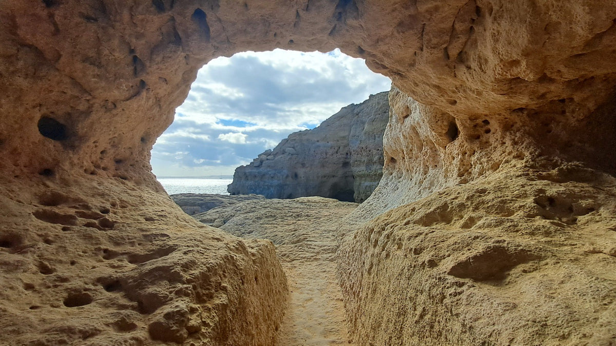 Rocky coastal cave framing blue ocean water and sunlit cliffs beyond.