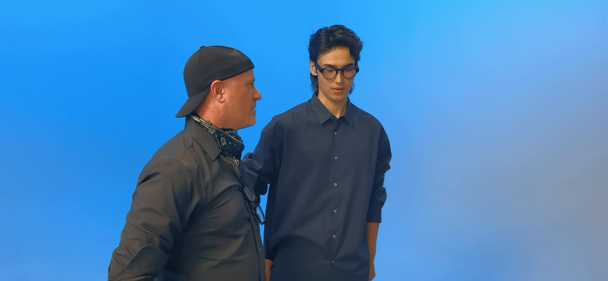 Crew lead standing beside a male model in camera glasses during the blue-set campaign shoot.