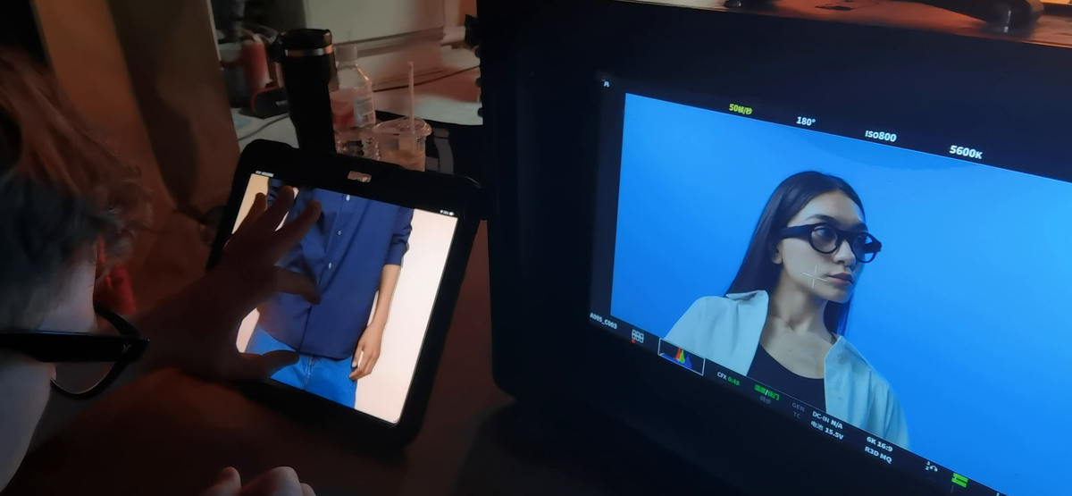 Production monitor showing a female model wearing 8ight camera glasses on a blue set.