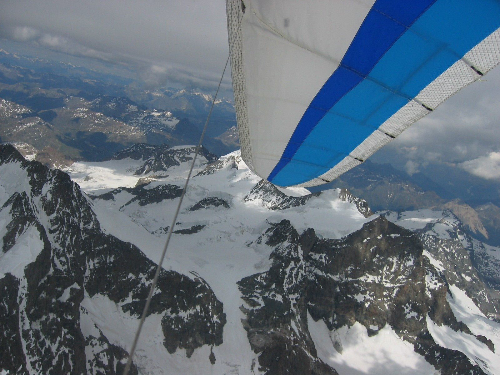 View past a blue and white hang glider wing above snow-covered alpine peaks