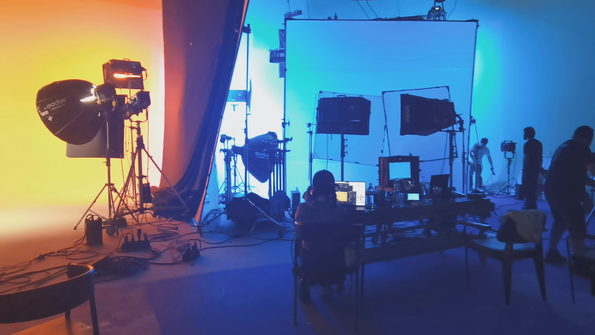 Wide orange-and-blue campaign set with studio lights, production monitors, tables, and crew.