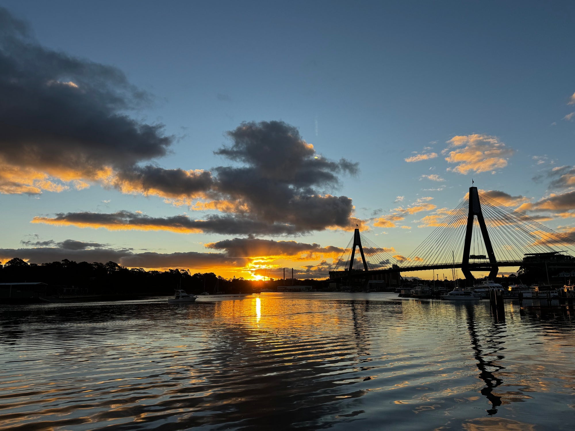 High-contrast waterfront sunset reflected beneath a cable-stayed bridge
