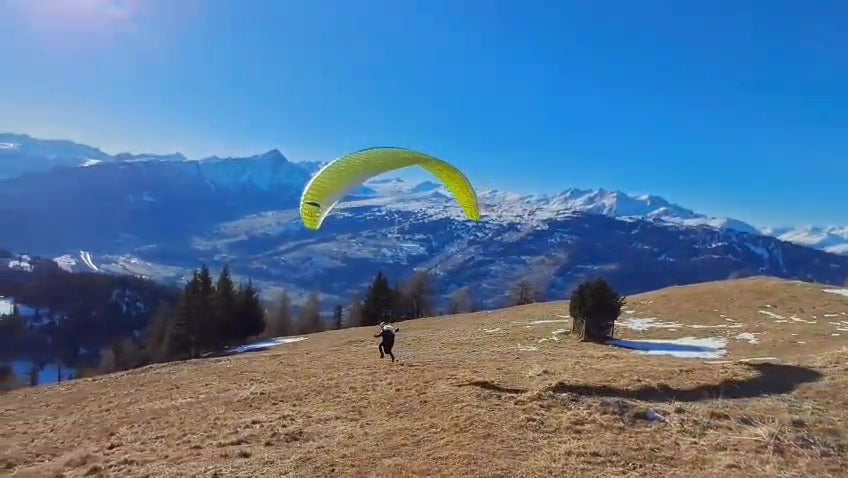 Yellow paraglider preparing to launch above an alpine landscape